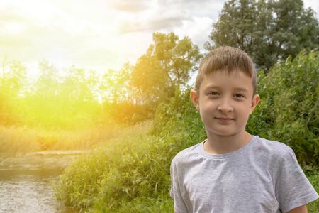 Portrait of happy smiling preteen boy outdoors in summertime, green nature and sunlight on backgroundの写真素材