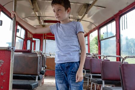 A 10 years boy riding in a old vintage bus, he is sad because his poor life and the bus moving going on a dirty country road.の写真素材