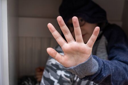 A teenage boy sitting under the table and hiding his face with a hand.の写真素材