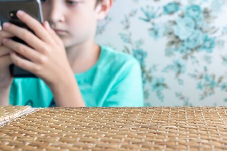 A teenage boy with serious face playing online games using smartphone while sitting in a restaurant,...