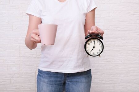 Woman holding a cup of coffee and alarm clock showing 7 am in hands, ready for work concept.