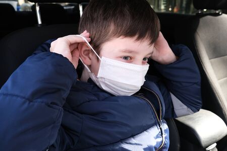 A teenage boy in car putting on white protective surgical medical face mask as a protection against...