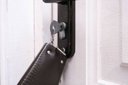 A bunch of keys with a leather key case inserted in a keyhole in order to open or lock a white...