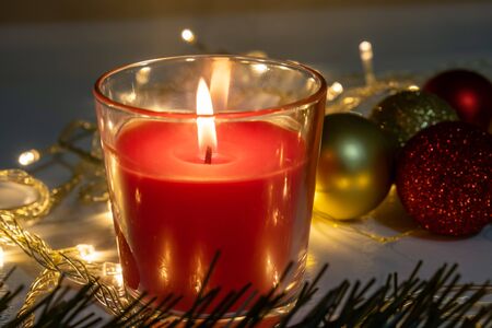 Red christmas candle, burning candle fire on a table with holiday garland and pine tree decorations and balls.の写真素材