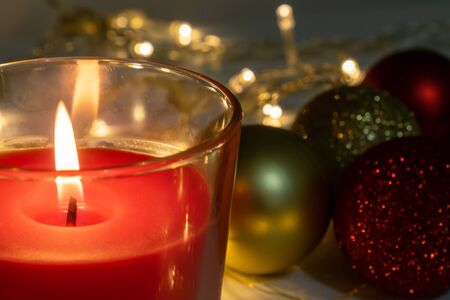 Red christmas candle, burning candle fire on a table with holiday garland and pine tree decorations and balls.の写真素材