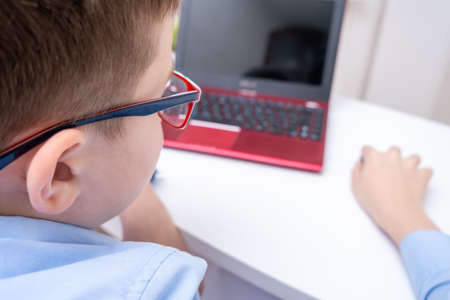 A school boy sitting by the table with a laptop and doing homework, e-learning, online education and home school concept.の写真素材