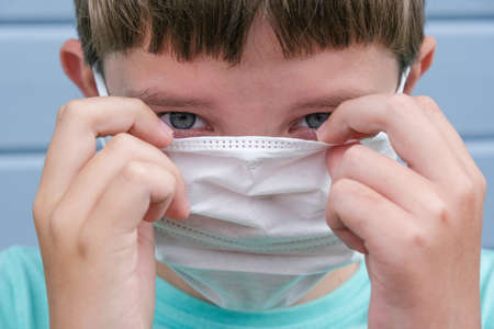 A suspicious boy wearing, putting on white protective surgical medical mask to prevent infection...