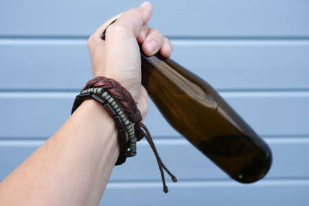 A hand of a hippie, hipster holding a bottle of alcohol, beer. Young people with alcohol addiction...