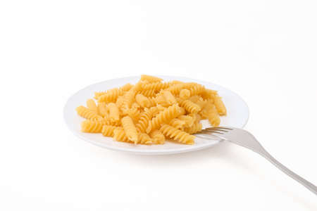 Raw uncoocked pasta fusilli in white ceramic plate with a folk isolated on white, italian cousine conceptの写真素材