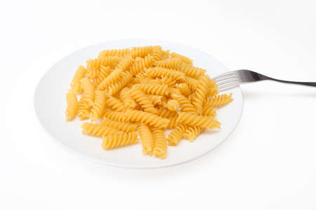 Raw uncoocked pasta fusilli in white ceramic plate with a folk isolated on white, italian cousine conceptの写真素材
