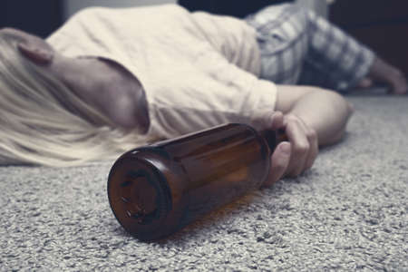 Woman lying on the floor with an empty alcohol bottle ans sleeping, overdosage and female alcoholism concept.の写真素材