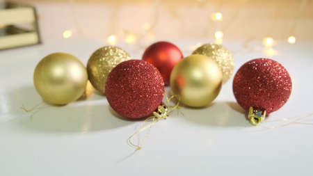 Red and golden christmas balls decorated with glitter close up on white table with a garland on...