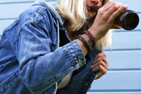 A drunked woman dressed punk, informal drinking beer from a brown bottle, alcohol overdosage and addiction concept.の写真素材