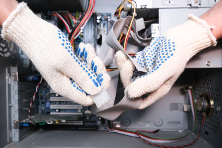 A technician in gloves holding cables of a broken computer in order to find a breakdown.の写真素材
