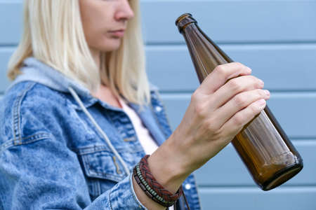 Woman dressed punk, infirmal holding a bottle of beer against blue wooden plank wall, abuse and female alcohol addiction concept.の写真素材