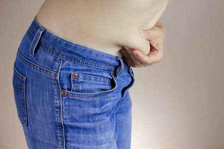 Hands of a overweighted woman holds a fold of excess fat on the stomach, slimming and losing weight concept.の写真素材