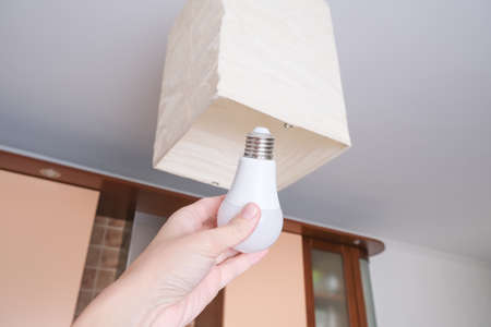 Female hand holding a led light bulb to change, replace it at home, screwing in the bulb into a lamp...