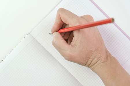 Female hands holding red pencil and writing something in a notebook, goal setting and planning...