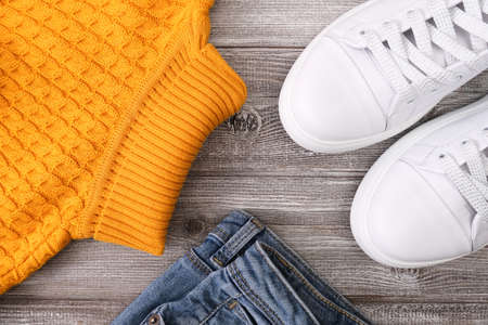 Yellow warm pullover for cold autumn, jeans denim and winter weather with white casual leather sneakers on wooden backgroundの写真素材