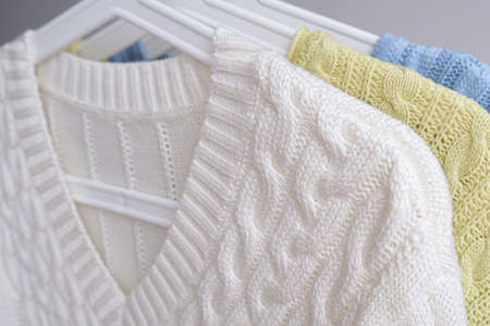 Various cable knit woolen warm winter sweaters or pullovers on hanger rack in a clothes store or at a wardrobe, pastel colorsの写真素材