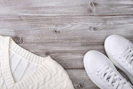 White warm pullover for cold autumn and winter weather with white casual leather sneakers on wooden background, copy space, flat layの写真素材