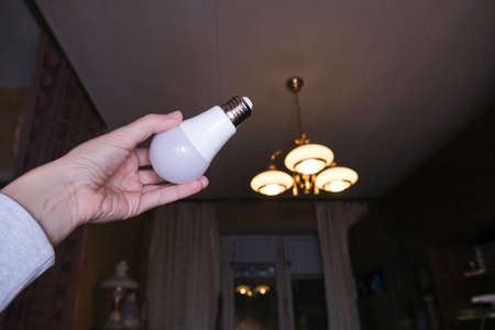 Female hand holding a led light bulb to change, replace it at home, screwing in the bulb into a lamp...