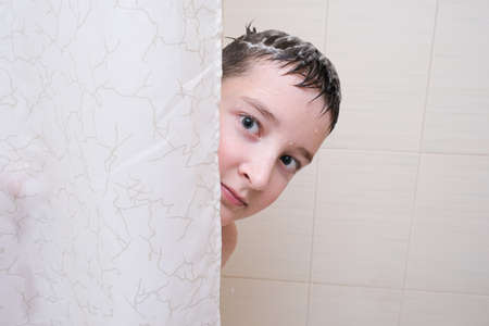 A boy teenager peeping out from behind a curtain in shower, bathroom, his face is wet and fair is foamy.の写真素材