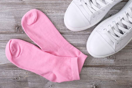 White leather sneakers and pink cotton socks on wooden background, a set for walking and workout.の写真素材