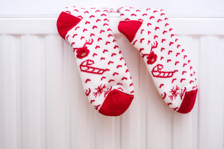 White and red christmas socks hanging on warm central heat radiator, winter holiday home moodの写真素材