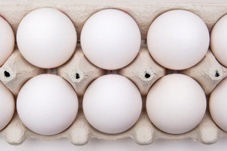 White eggs in recycled carton pressed box container on white table, close up top view