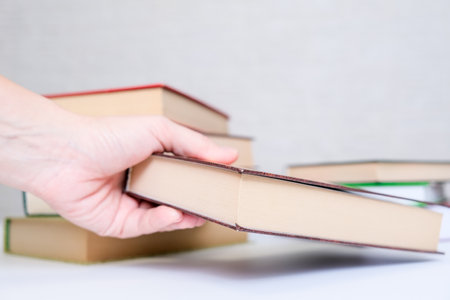 A hand taking a book from a stack, pile, choosing and selecting books for reading and education