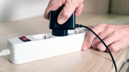 A hand inserting a plug into electrical power strip close up, charging devices concept