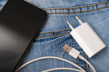 Charging smartphone concept, a usb cable for charging devices, gadgets with adapter plug and a phone on a jeans backgroundの写真素材