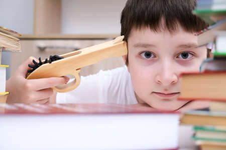 Too much information concept, a boy kid sitting at the desk and holding a toy gun, tired of reading and homeworkの写真素材