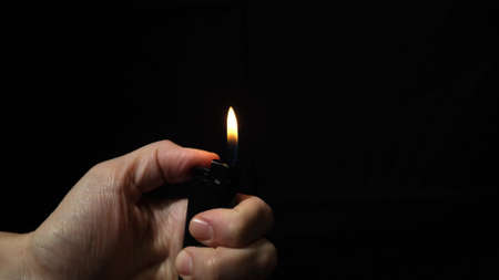 Hand burning flame with a lighter in the dark, black night background, portable device used to create a flameの写真素材