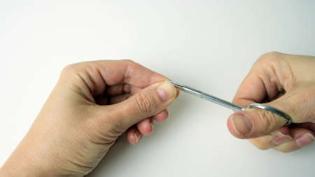 Hand of a woman cutting nails with scissors and making manicure by herself at home