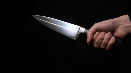 A hand of a murderer or robber holding a big knife and showing a sharp blade at night close up