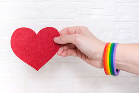 A woman wearing lgbtq rainbow bracelet holding a heartの写真素材
