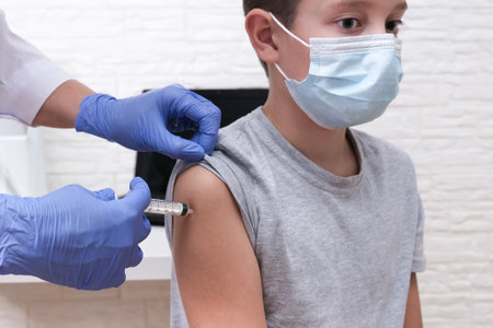 A boy at school getting vaccinated from covid-19, receiving a vaccine from sars-cov-2 virusの写真素材