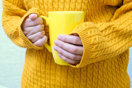 Woman in yellow cozy knitted sweater holding a big cup of hot beverage, autumn fall conceptの写真素材