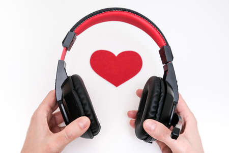 Hands holding stereo headphones and a red heart as a love music concept