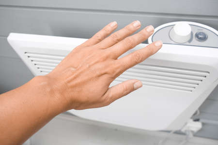 A hand checking temperature of heating convector on the wall, air heating the house in fall and winterの写真素材