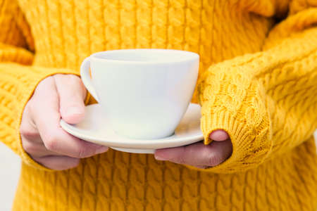 Unrecognizable woman in yellow warm knitted sweater holding a white cup of cofffeの写真素材