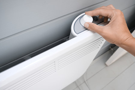 Hand regulating, setting temperature on electric convector, heater thermostate in the room in winter, climate control, home heating and energy saving conceptの写真素材