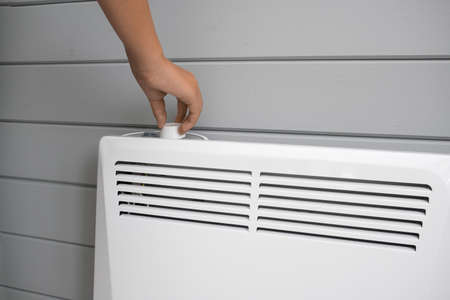 Hand regulating, setting temperature on electric convector, heater thermostate in the room in...