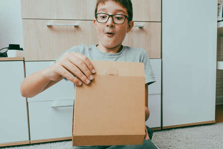 Excited boy sitting on a carpet and opening a box, a parcel, unboxing and unpacking conceptの写真素材
