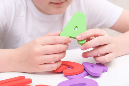 A kid learning letters and alphabet, he is sitting at a table and holding colorful foam letters in handsの写真素材