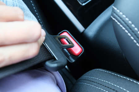 Woman holding a buckle of a safety belt in hand and fastening a seatbelt, car safety and driver...