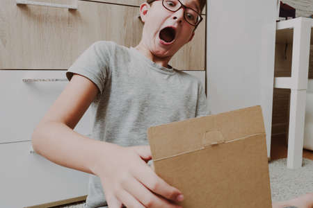 Excited boy sitting on a carpet and opening a box, a parcel, unboxing and unpacking concept.の写真素材