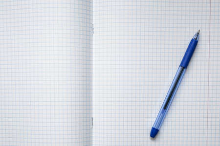 A blue ball pen lying on a blank checkered school notebook sheet, paper with copy space.の写真素材